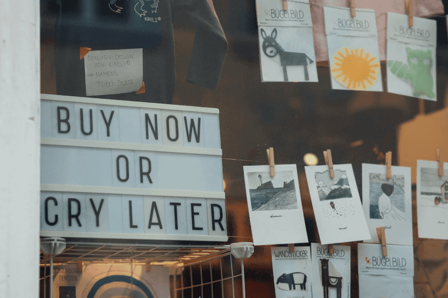 A CTA on a sign in a shop window that reads “Buy Now or Cry Later”