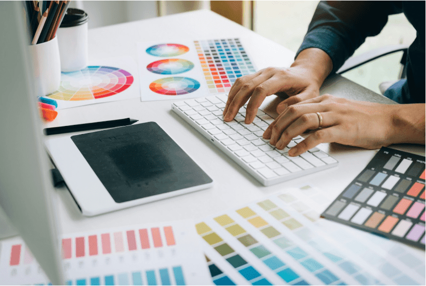 A designer works at a desk with sheets of color palettes around them