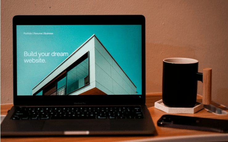 A laptop open on an aesthetic desk space, with the screen reading “Build Your Dream Website”