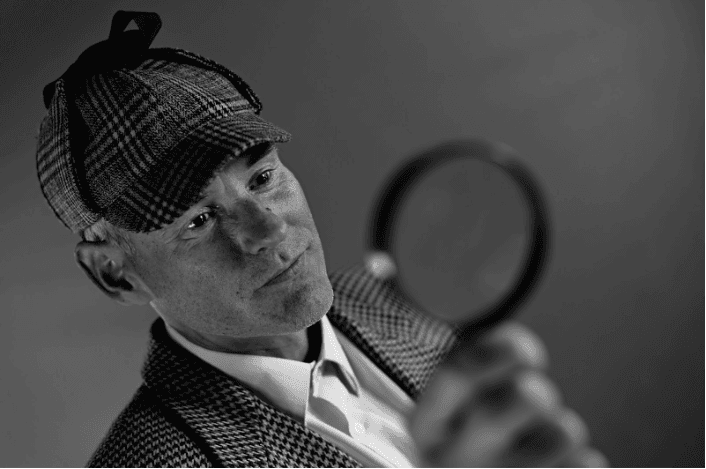An old-school looking detective in black and white with a magnifying glass