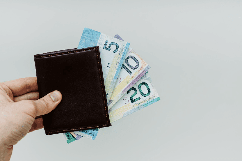 Someone holding a leather wallet with several Canadian Dollar notes spread out of it