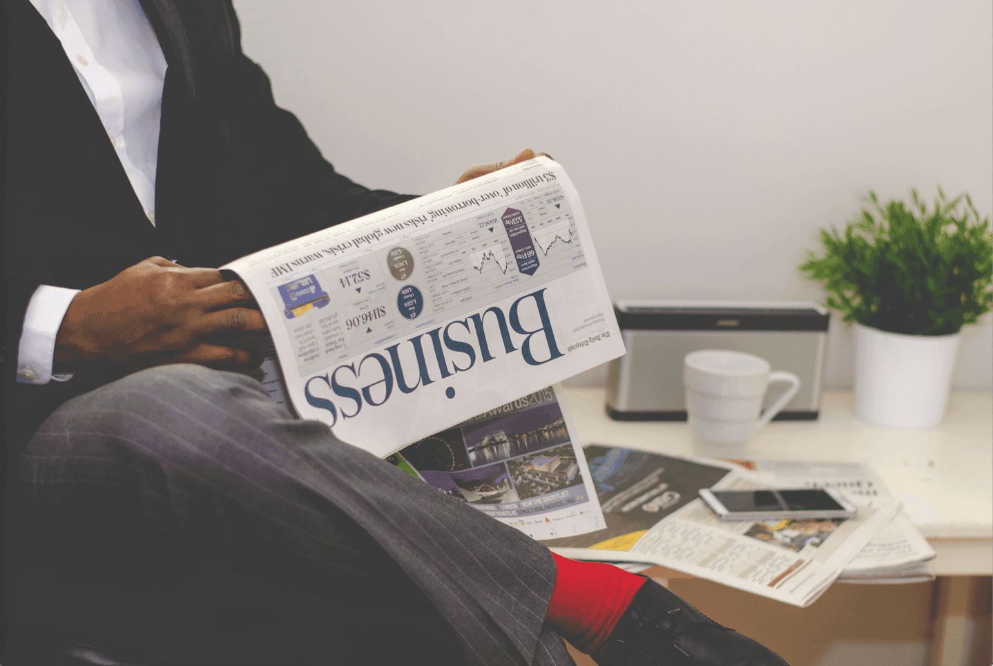 A man in a suit sits calmly, engrossed in reading the business newspaper, exuding a professional and focused demeanor..