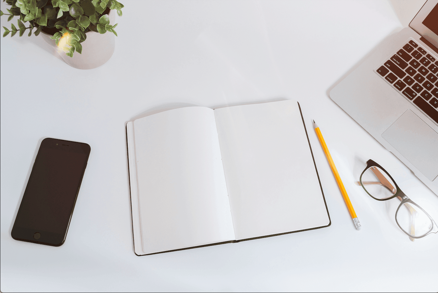 A clean and organized workspace on a white table, featuring a computer, notebook, pens, and minimal decor, exuding a modern and focused atmosphere.