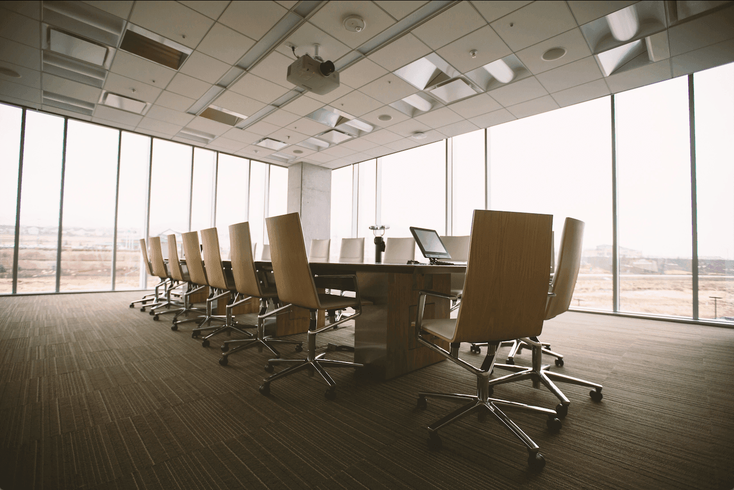 A spacious and modern conference room in an office setting, featuring a large table, sleek chairs, a projector, and glass windows that offer a professional and collaborative atmosphere.