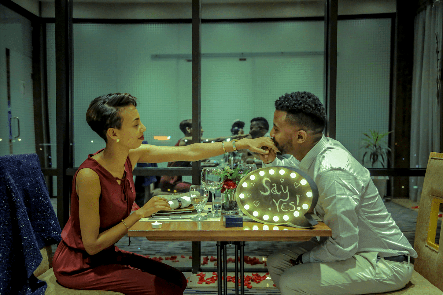 A man and woman enjoying dinner together, with a 'Say Yes' sign placed nearby, creating a joyful and celebratory atmosphere.