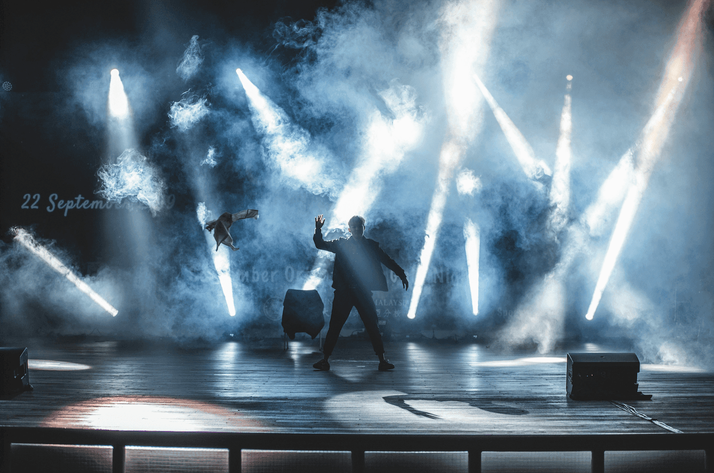 A man standing confidently on a stage, surrounded by dynamic lights and smoke, creating a dramatic and energetic atmosphere.