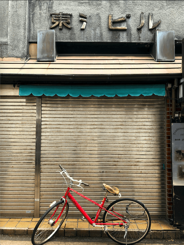 A red bike parked in front of a rustic wooden shed, adding a vibrant contrast to the earthy tones of the shed's weathered texture.
