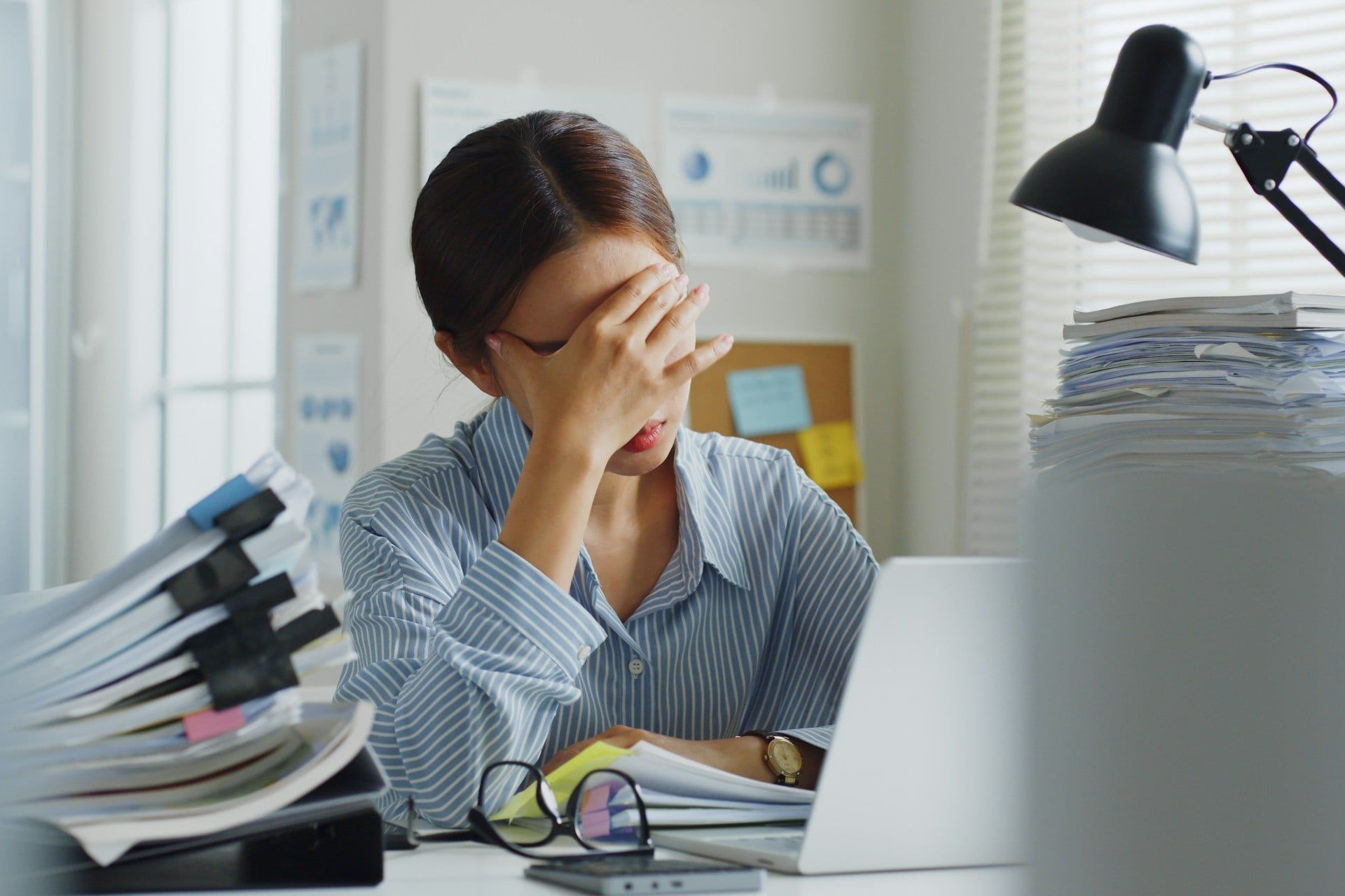 An Asian woman looks stressed sat at a desk dealing with a bad website experience and a big stack of paperwork