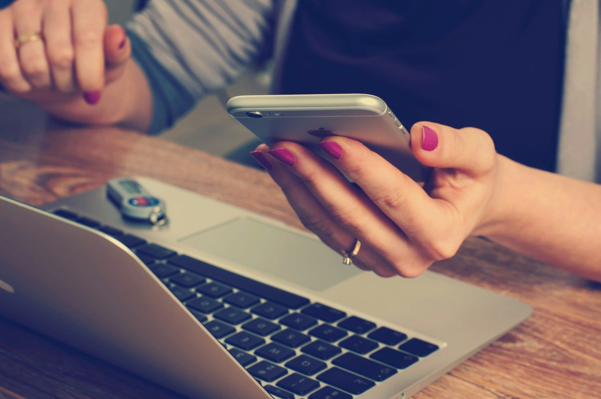 A woman sits at her laptop scrolling on websites on her iPhone