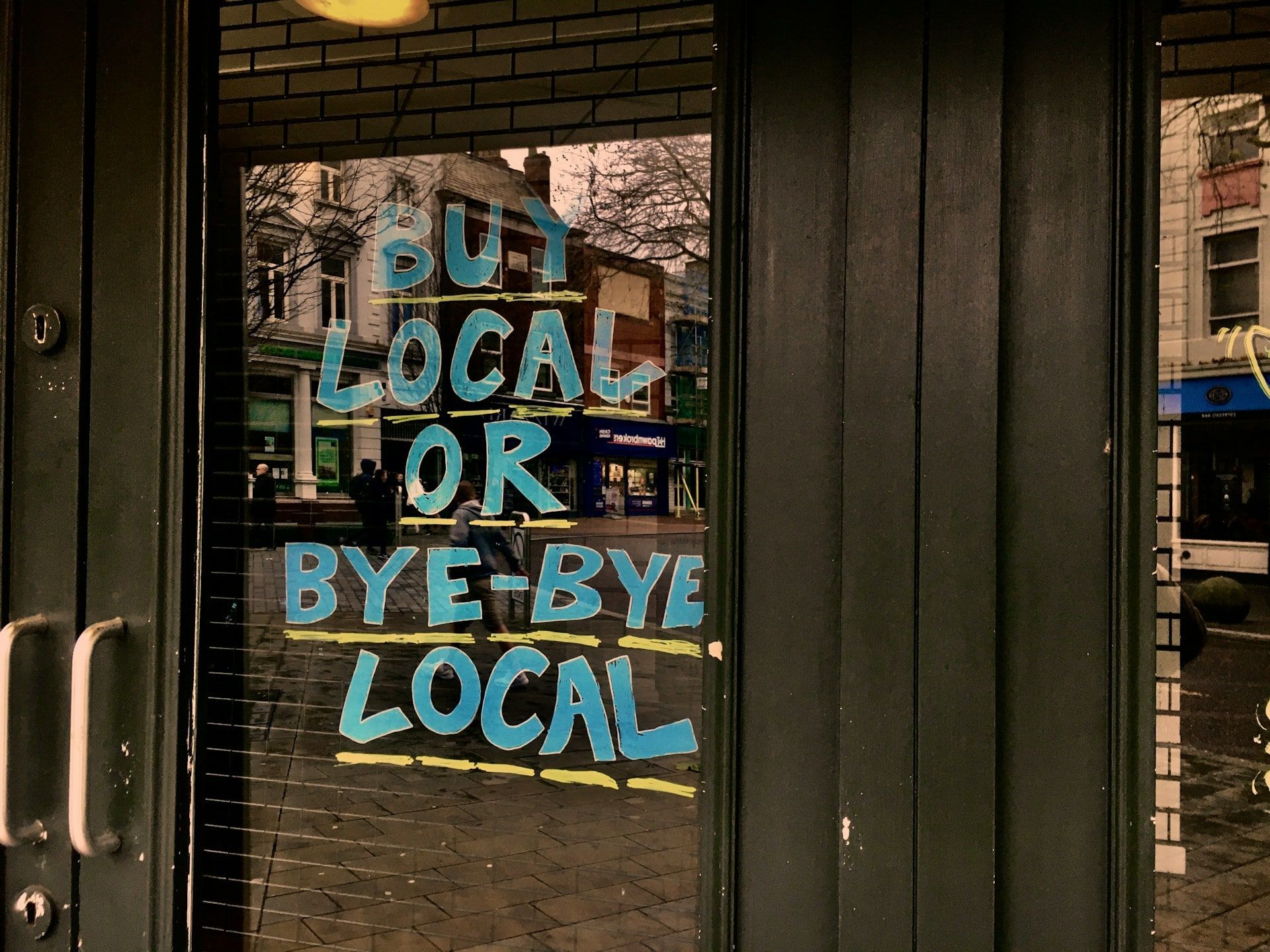 A hand-drawn sign in a shop window that reads “Buy local or bye-bye local”