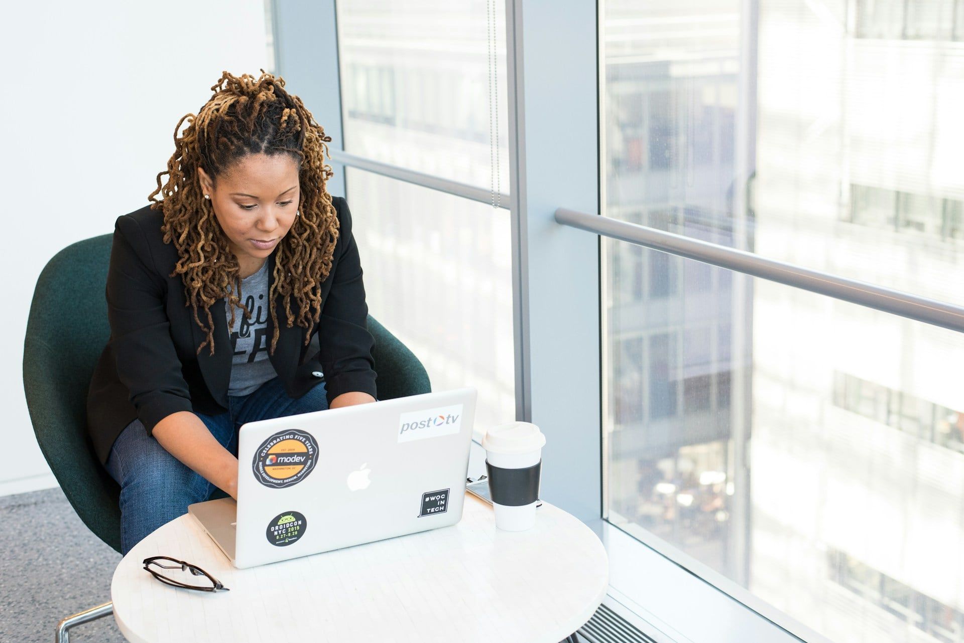 A female business owner sits working on her laptop by a big floor-to-ceiling window overlooking Edmonton city
