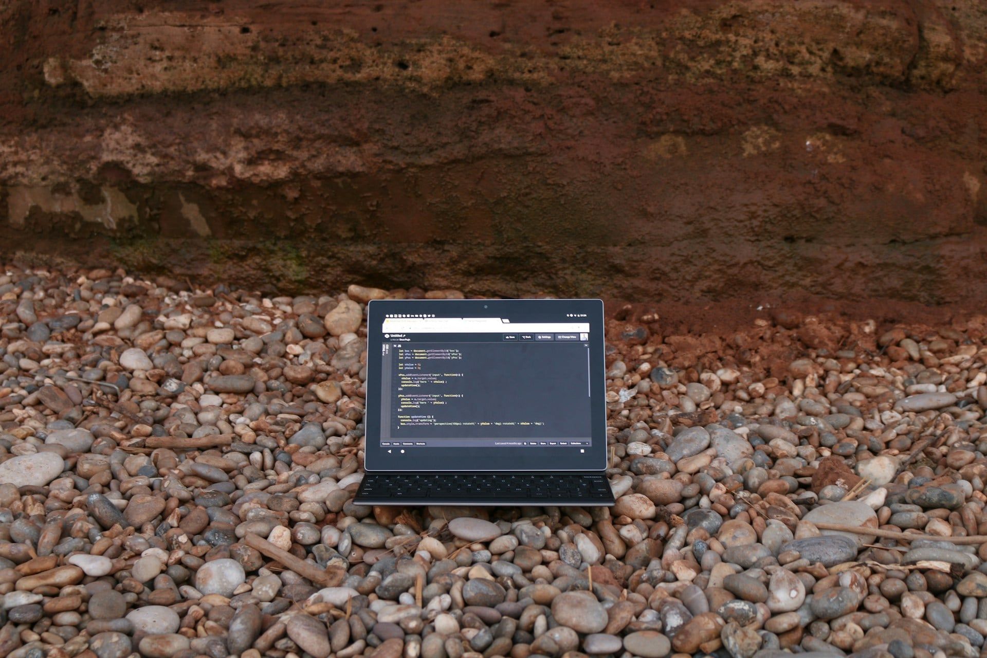 A laptop with website HTML code open on the screen positioned on a stony beach