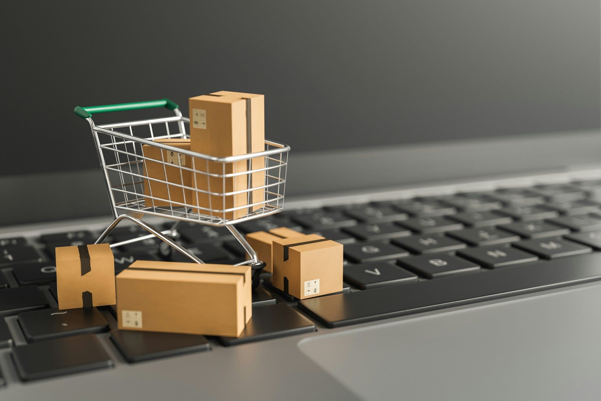 A close-up of a laptop with a small model shopping cart with boxes stacked around it, representing e-commerce shopping