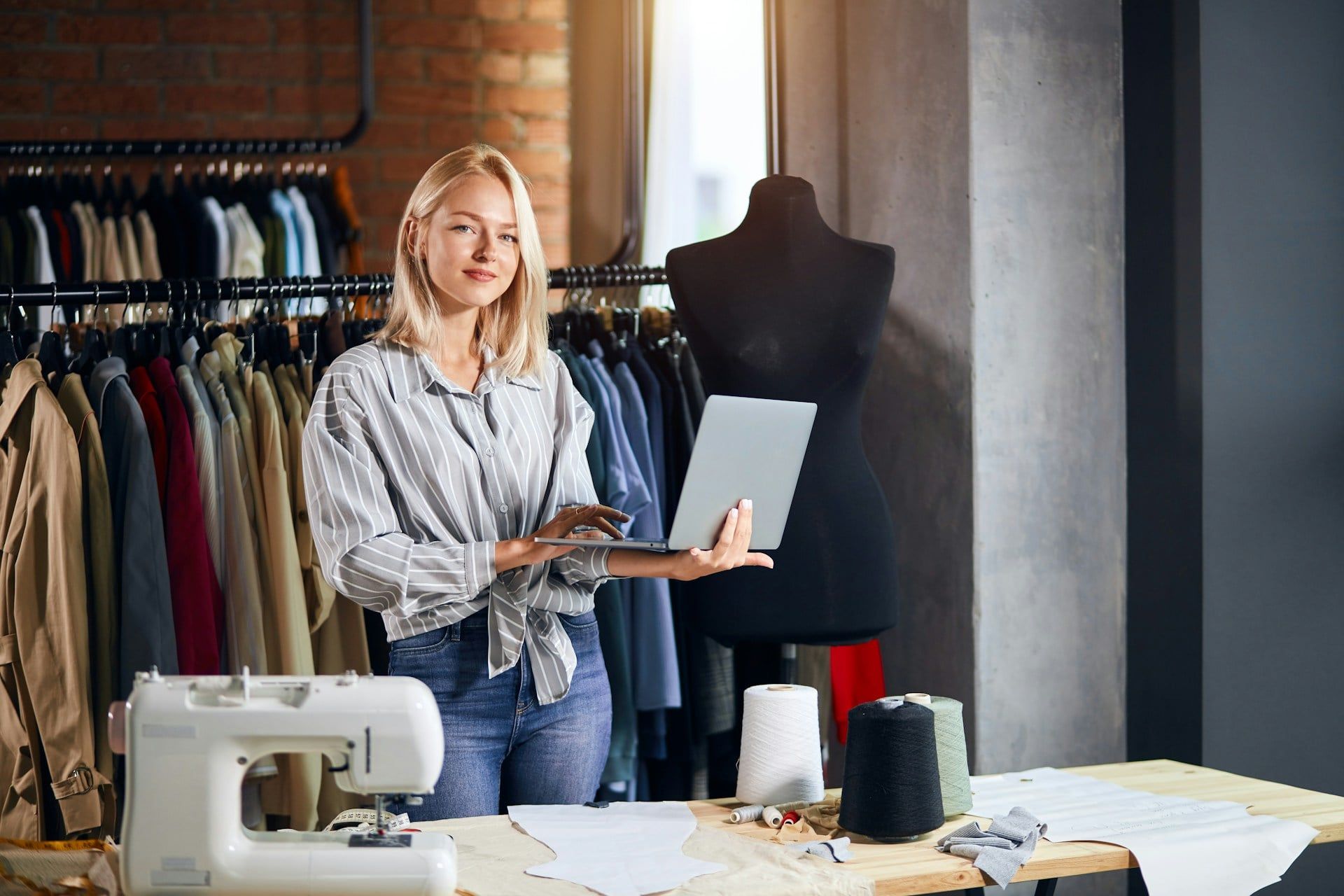A female Edmonton small business owner stands smiling in her store, holding her laptop