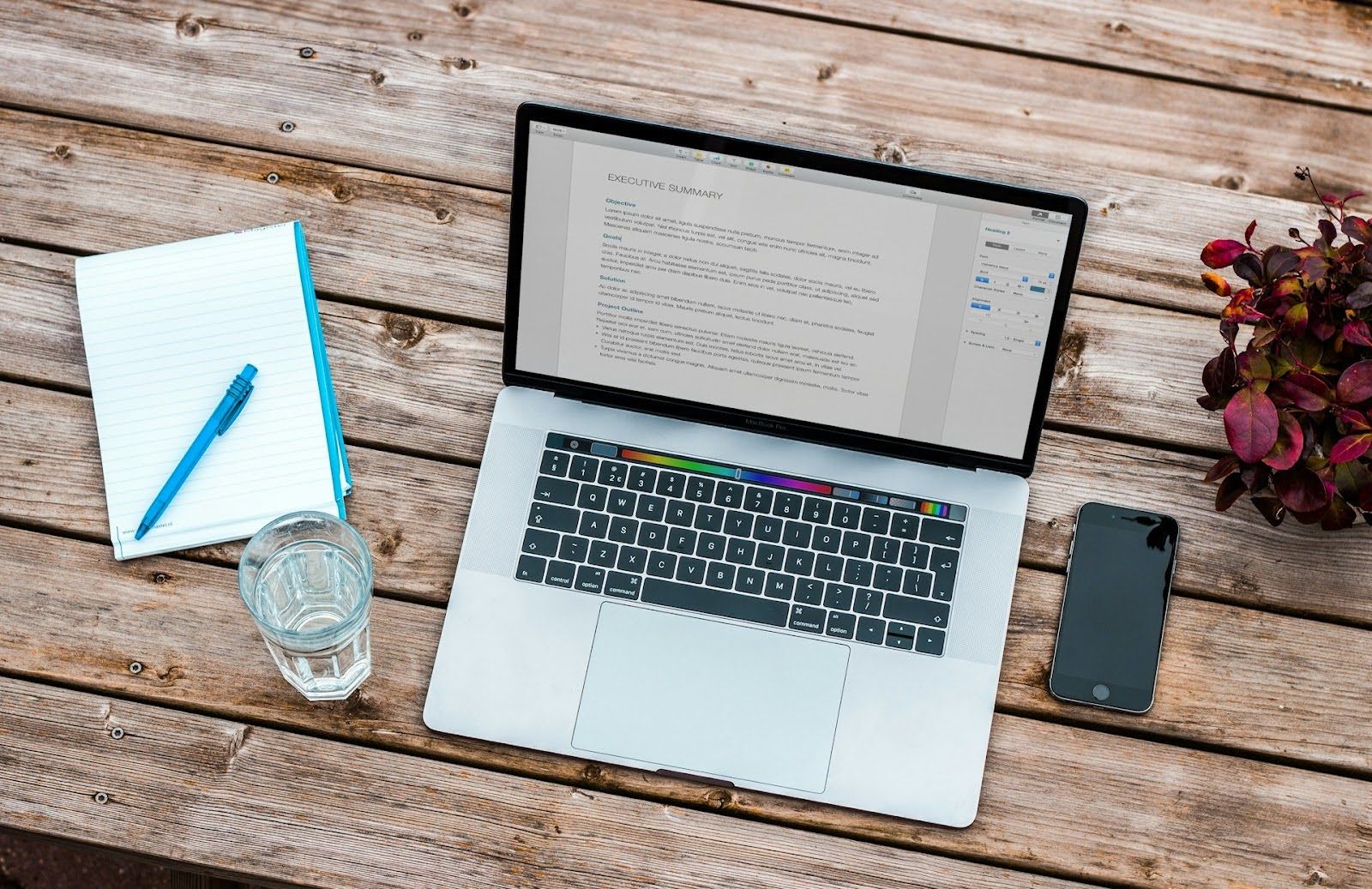 A wooden desk with a laptop, a notebook and pen, and a smartphone aesthetically positioned around