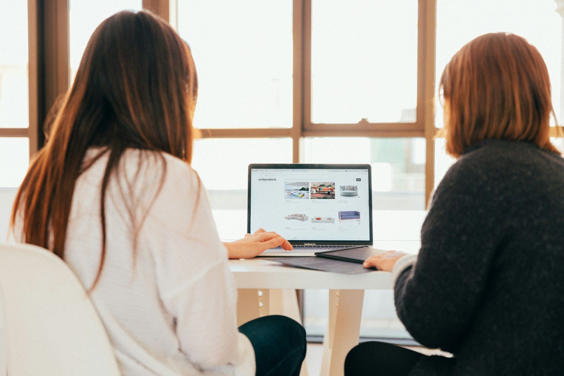 Two women sit at a desk reviewing their website