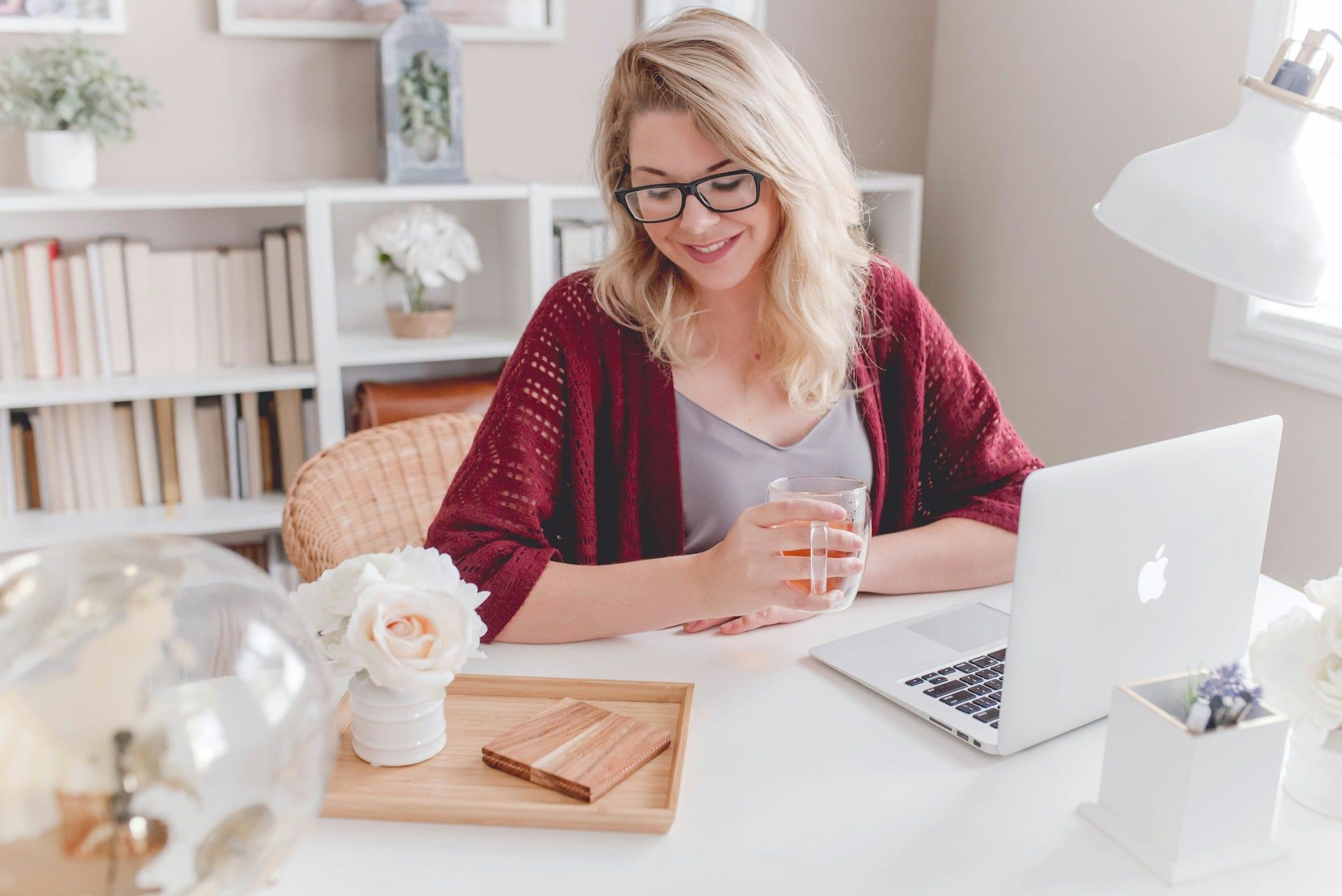 A woman sits at her desk working on her business while smiling and drinking tea