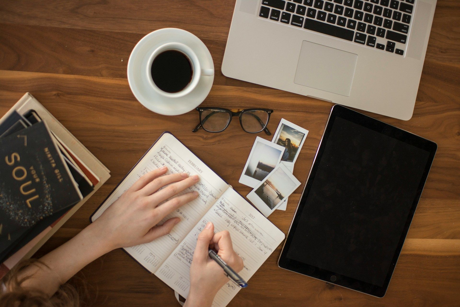 A top-down view of a desk with a computer, a few books, and an Edmonton small business owner making notes in a notebook