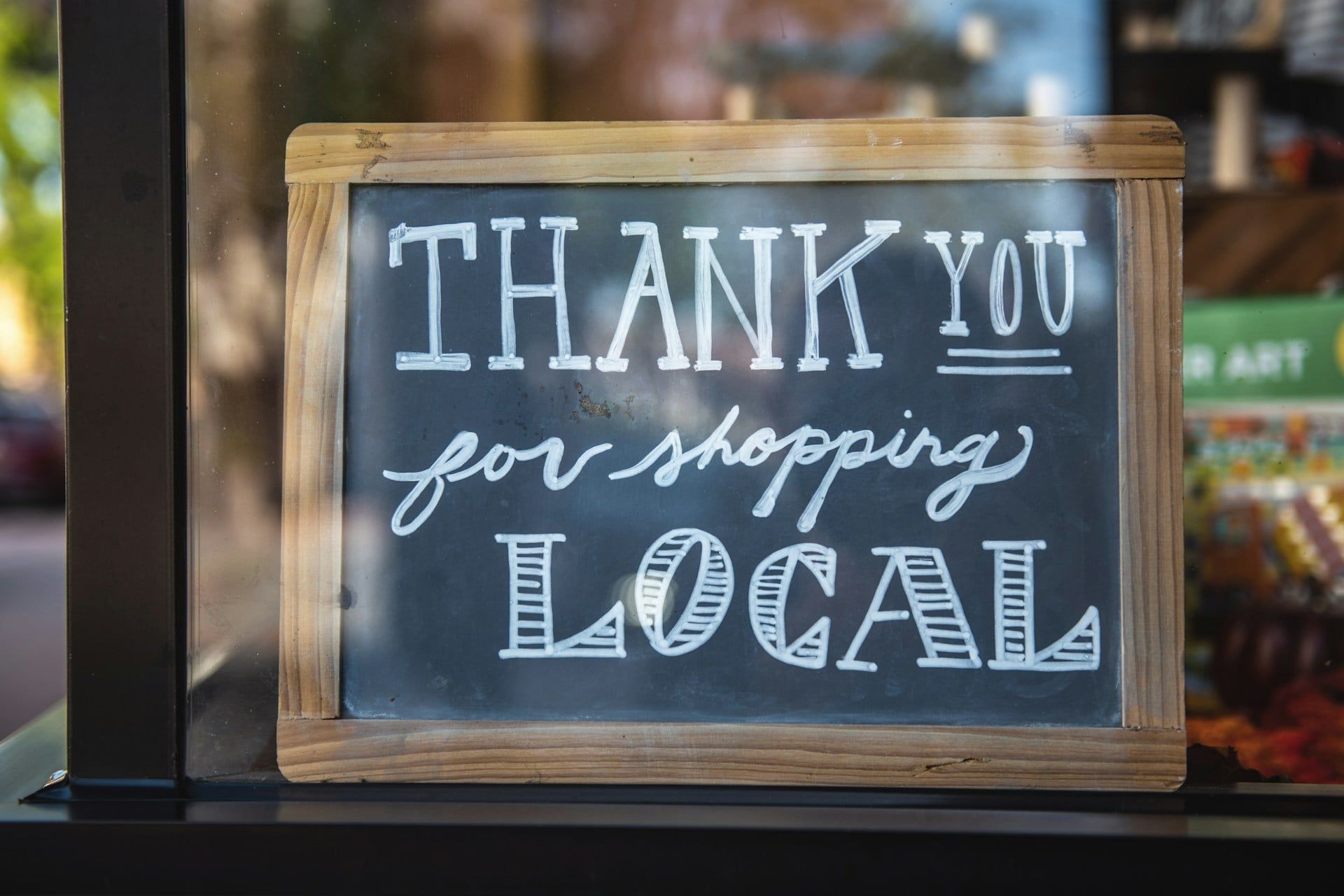 A wooden sign in a business window that reads “Thank for shopping local”